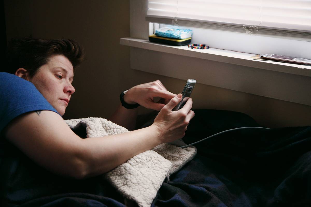 Woman using sleep schedule app on smartphone while adjusting bedroom lighting for better sleep hygiene